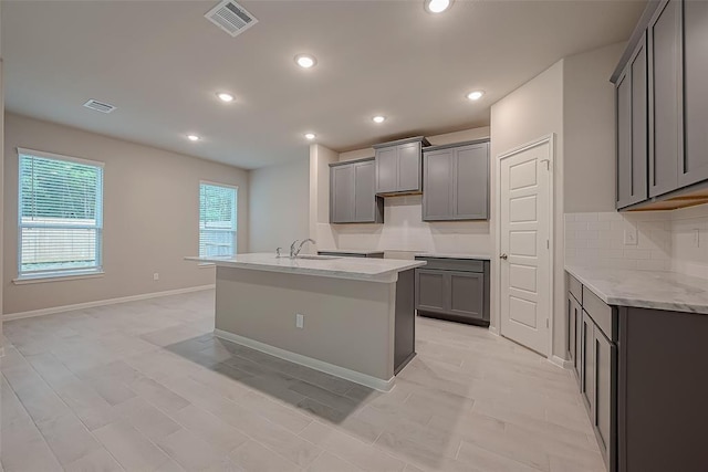 kitchen with a kitchen island with sink, visible vents, gray cabinets, and decorative backsplash