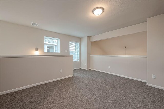 spare room with visible vents, baseboards, and dark colored carpet