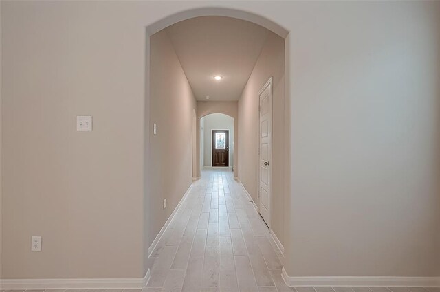 hall with baseboards, arched walkways, and light wood-type flooring