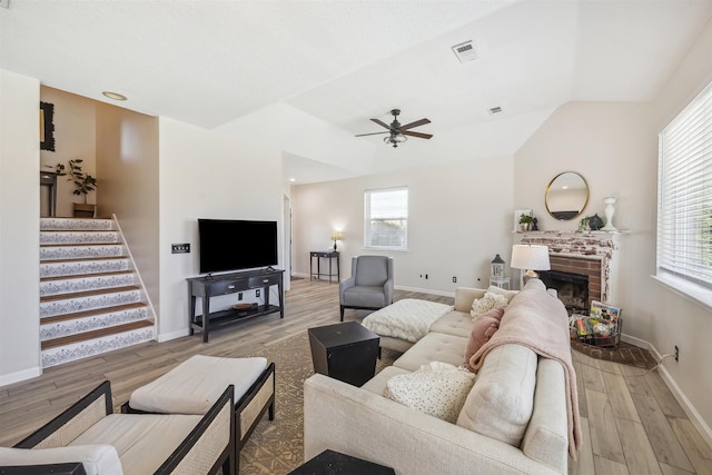 living area featuring a wealth of natural light, stairway, a brick fireplace, and wood finished floors