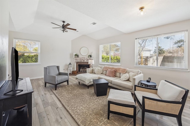 living room with light wood-type flooring, visible vents, a fireplace, baseboards, and vaulted ceiling