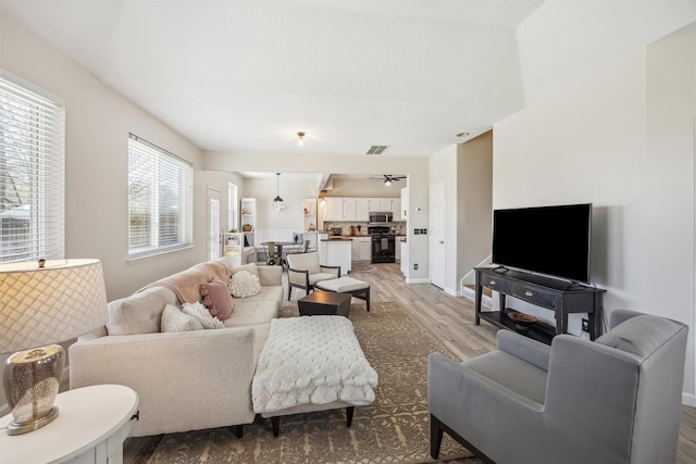 living room with light wood-style flooring, baseboards, visible vents, and ceiling fan