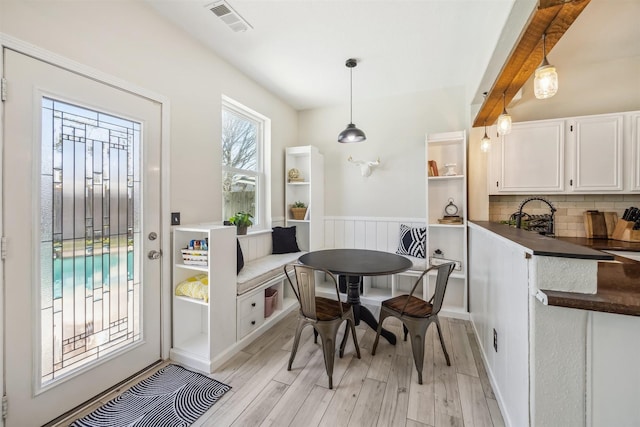 dining area with visible vents, wainscoting, light wood-type flooring, and beamed ceiling