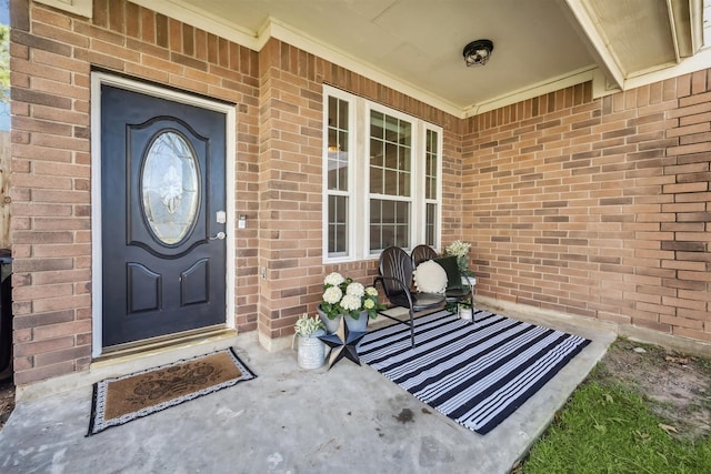 view of exterior entry featuring a porch and brick siding