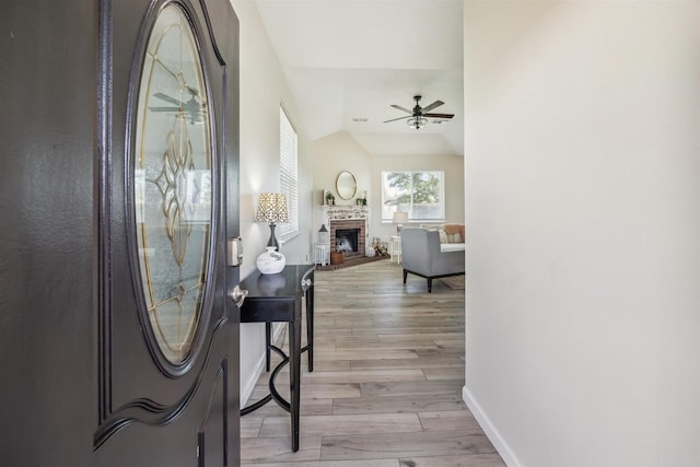 foyer entrance with light wood finished floors, a brick fireplace, baseboards, ceiling fan, and lofted ceiling