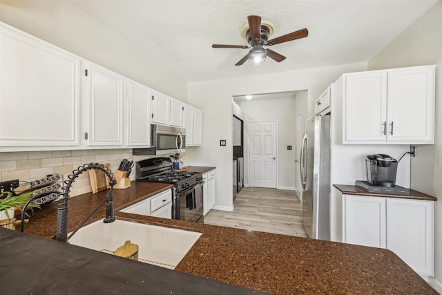 kitchen with a sink, backsplash, white cabinetry, stainless steel appliances, and dark stone counters