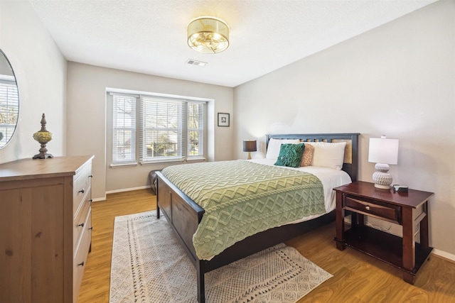 bedroom featuring light wood-style flooring, multiple windows, baseboards, and visible vents