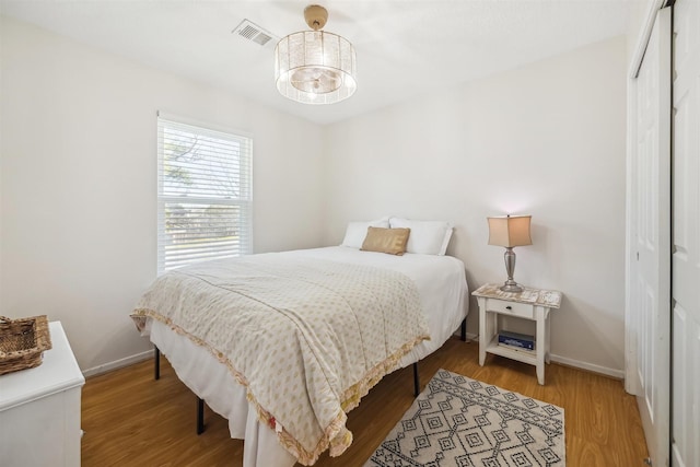 bedroom with wood finished floors, visible vents, a closet, and baseboards