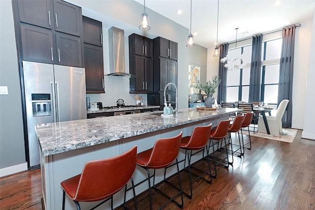 kitchen with a center island with sink, stainless steel appliances, dark wood-style floors, and wall chimney exhaust hood