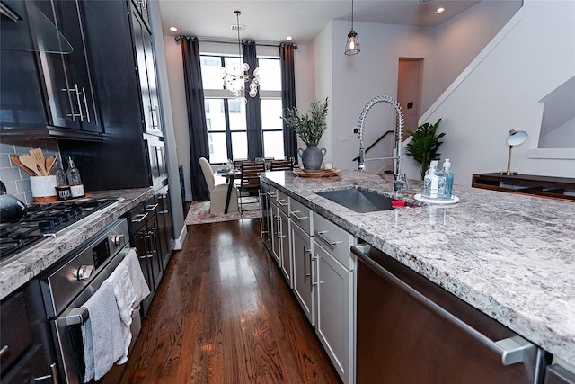 kitchen featuring light stone countertops, dark wood-style floors, a sink, appliances with stainless steel finishes, and pendant lighting