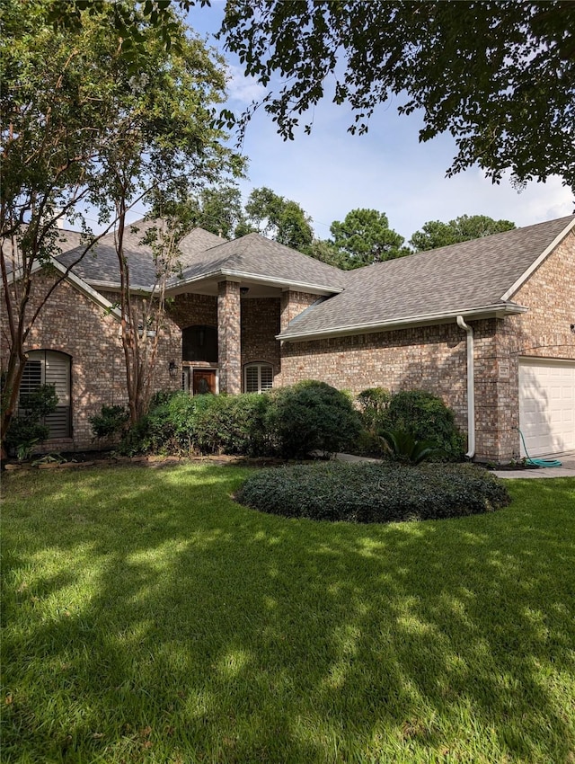 view of front of home with brick siding, an attached garage, a front lawn, and a shingled roof