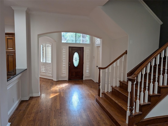 entrance foyer with wood finished floors, arched walkways, crown molding, baseboards, and stairs