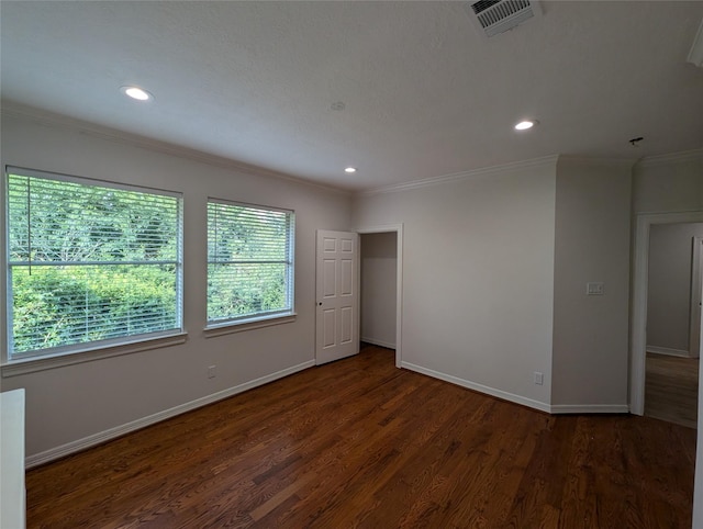 empty room with a wealth of natural light, visible vents, ornamental molding, and wood finished floors