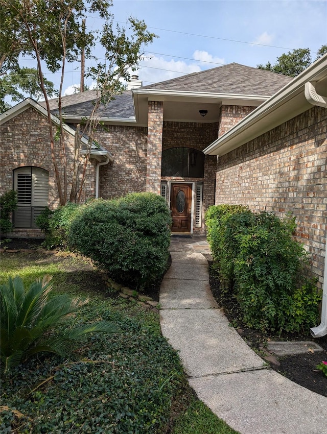 doorway to property with brick siding and roof with shingles