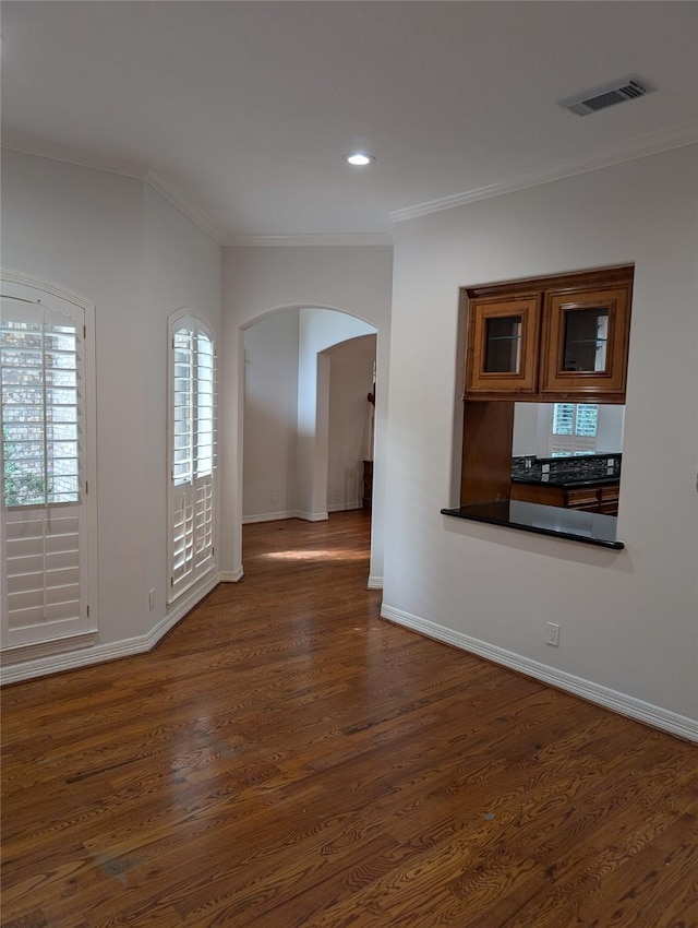 unfurnished living room with visible vents, dark wood-type flooring, ornamental molding, arched walkways, and baseboards