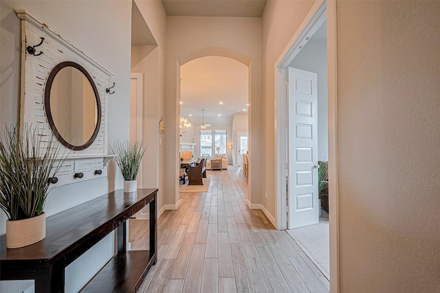 corridor with arched walkways, light wood finished floors, and baseboards