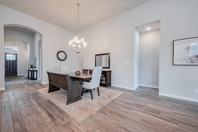 dining room with a chandelier, arched walkways, baseboards, and wood finished floors