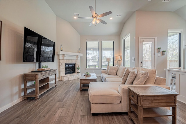 living room featuring wood finished floors, visible vents, lofted ceiling, ceiling fan, and a stone fireplace