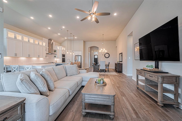 living room featuring ceiling fan with notable chandelier, arched walkways, light wood finished floors, baseboards, and vaulted ceiling