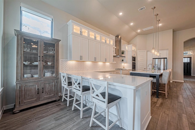 kitchen with visible vents, wall chimney range hood, a kitchen bar, light countertops, and appliances with stainless steel finishes