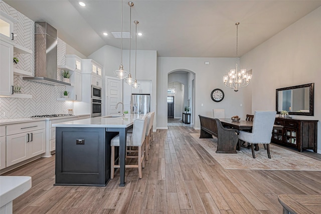 kitchen featuring a sink, stainless steel appliances, arched walkways, wall chimney exhaust hood, and light countertops