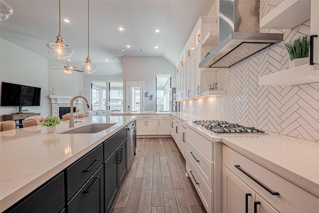 kitchen featuring ceiling fan, wall chimney range hood, dark cabinetry, stainless steel appliances, and a sink