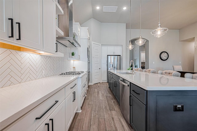 kitchen featuring visible vents, a sink, decorative backsplash, appliances with stainless steel finishes, and wall chimney exhaust hood