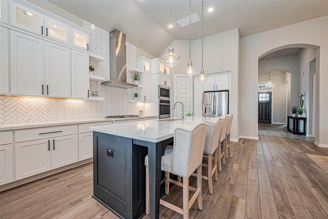 kitchen with tasteful backsplash, light countertops, appliances with stainless steel finishes, arched walkways, and wall chimney exhaust hood