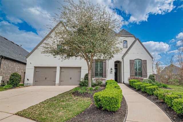 french country home with an attached garage, brick siding, and driveway