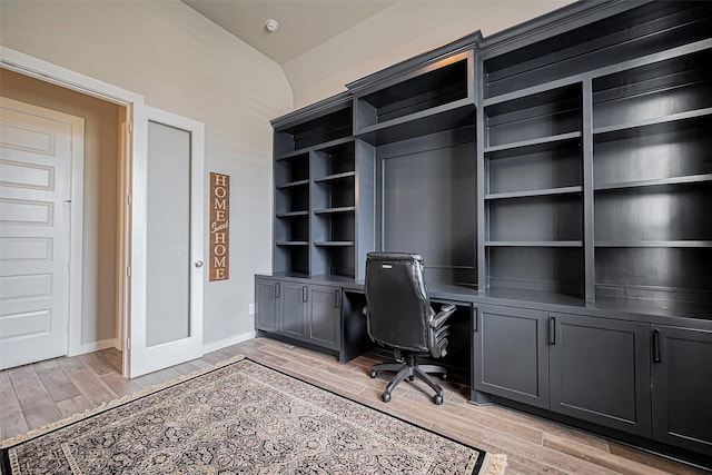 unfurnished office featuring baseboards, built in desk, and wood finish floors