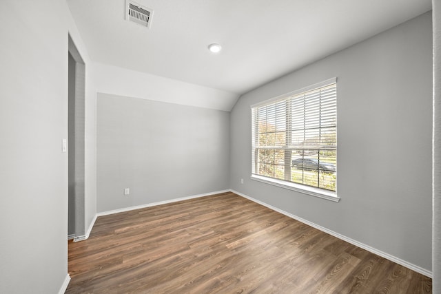 spare room featuring vaulted ceiling, baseboards, dark wood-style flooring, and visible vents