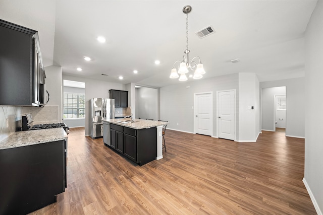 kitchen with visible vents, wood finished floors, appliances with stainless steel finishes, decorative backsplash, and dark cabinets