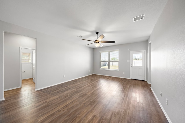 unfurnished living room with ceiling fan, visible vents, baseboards, and dark wood-style floors