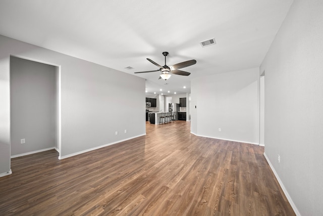 unfurnished living room featuring visible vents, baseboards, a ceiling fan, and dark wood-style flooring