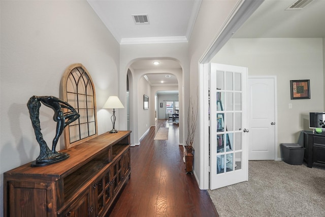 hall with dark wood finished floors, crown molding, arched walkways, and visible vents