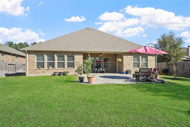 rear view of house with brick siding, a patio, a fenced backyard, and a lawn