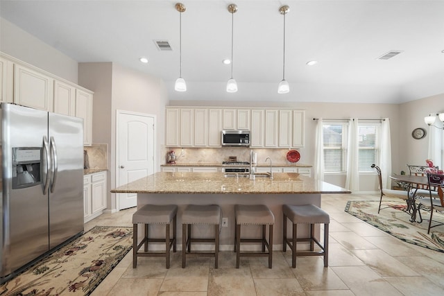 kitchen featuring light stone counters, stainless steel appliances, a kitchen island with sink, and decorative backsplash