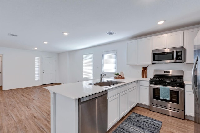 kitchen featuring light wood finished floors, a peninsula, stainless steel appliances, white cabinetry, and a sink