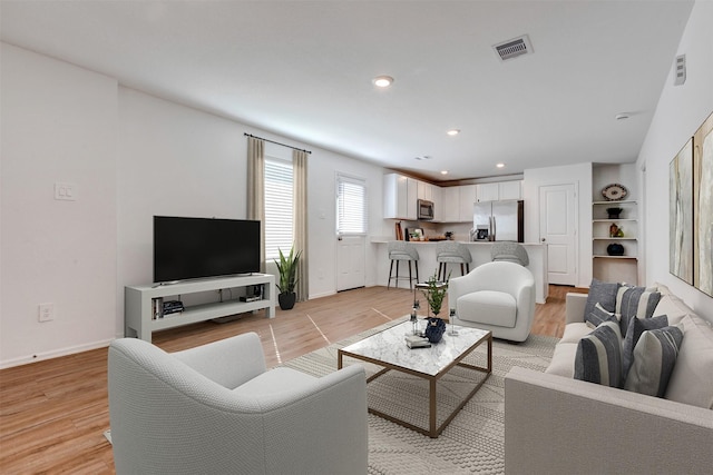 living room with light wood-type flooring, visible vents, baseboards, and recessed lighting