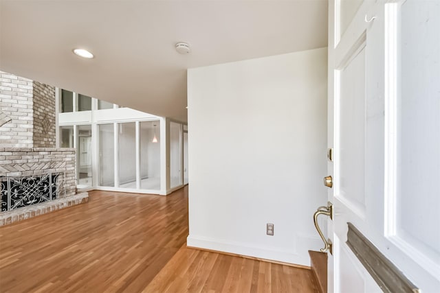 unfurnished living room featuring baseboards, a brick fireplace, and light wood finished floors