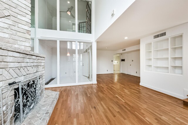 unfurnished living room featuring visible vents, built in features, wood finished floors, baseboards, and a brick fireplace