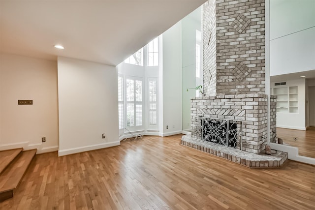 unfurnished living room featuring built in shelves, a brick fireplace, baseboards, a high ceiling, and wood finished floors