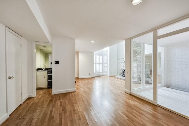 empty room with brick wall, baseboards, light wood-type flooring, expansive windows, and a sink