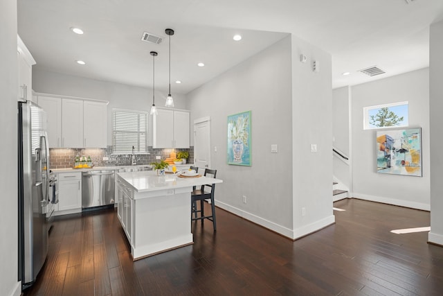 kitchen featuring stainless steel appliances, a breakfast bar area, light countertops, decorative backsplash, and dark wood-style flooring