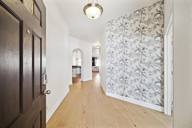 hallway with arched walkways, light wood-type flooring, and baseboards