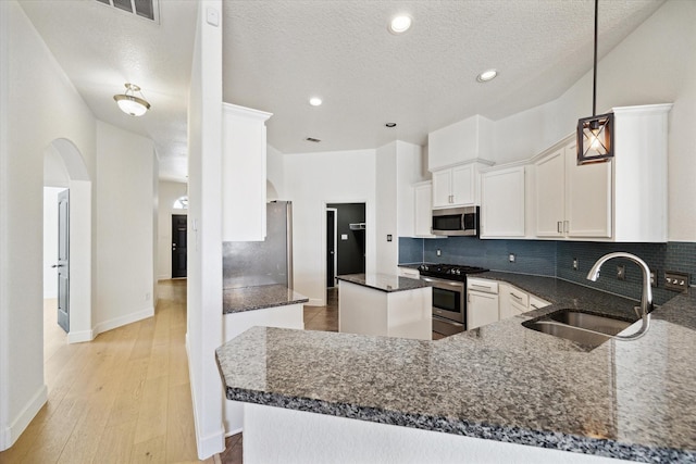 kitchen featuring a kitchen island, dark stone counters, a sink, appliances with stainless steel finishes, and backsplash