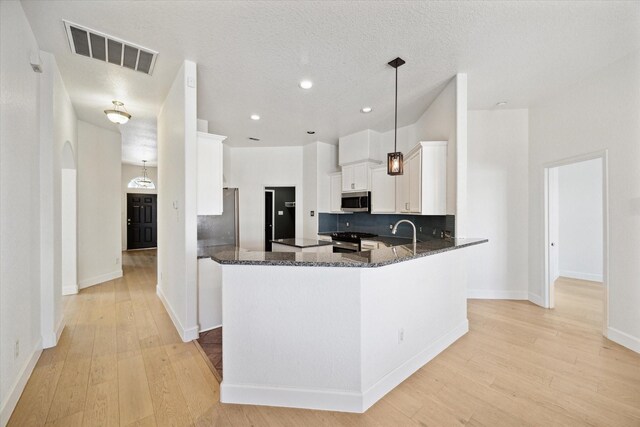 kitchen with visible vents, dark stone countertops, backsplash, stainless steel appliances, and light wood finished floors