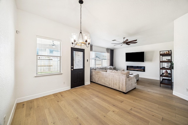 unfurnished living room featuring ceiling fan with notable chandelier, baseboards, and light wood-type flooring