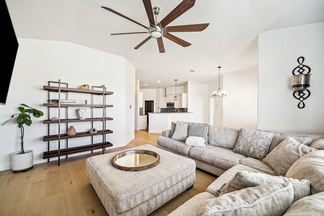 living room featuring ceiling fan with notable chandelier, vaulted ceiling, light wood-style floors, and baseboards