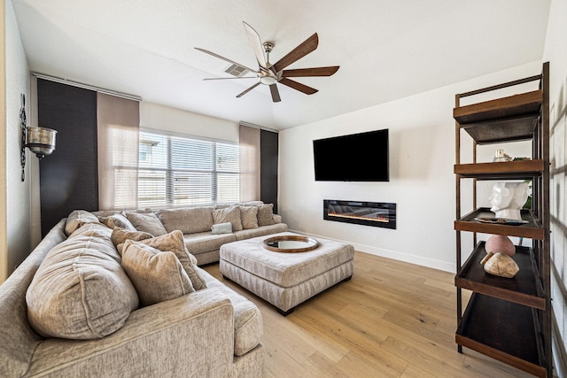 living room featuring baseboards, light wood-style floors, a glass covered fireplace, and a ceiling fan